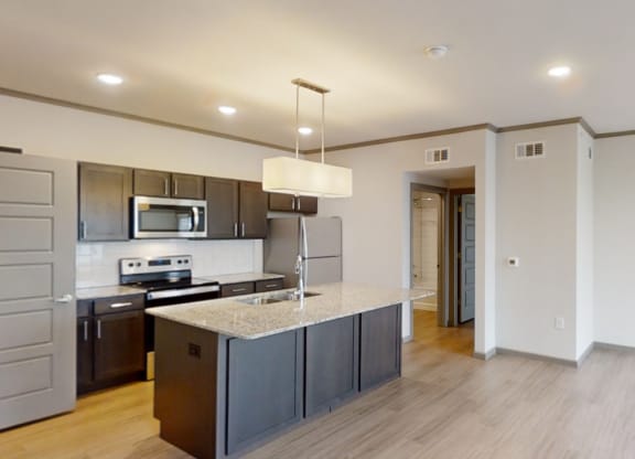 Modern kitchen here at 49 West Apartments view with a granite island, stainless steel appliances, and dark cabinetry. Bright lights create a welcoming, spacious atmosphere.
