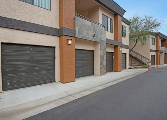 Aspire at Pinnacle Peak's modern apartment complex with beige and brown tones, featuring dark garage doors and stone accents. A tree and staircase add contrast. Calm atmosphere.