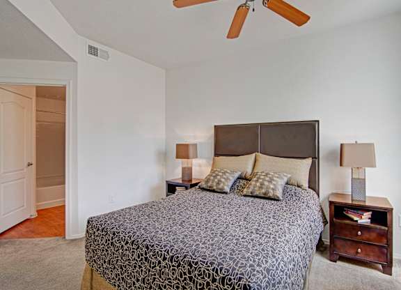 A bedroom with a patterned bedspread and a ceiling fan.