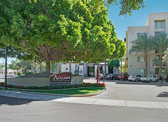 A street view of Acclaim Apartments with trees and cars.