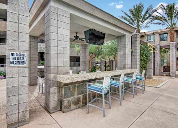 A patio area with a bar and chairs under a roof with a sign that says no alcohol, no glass, and no smoking.