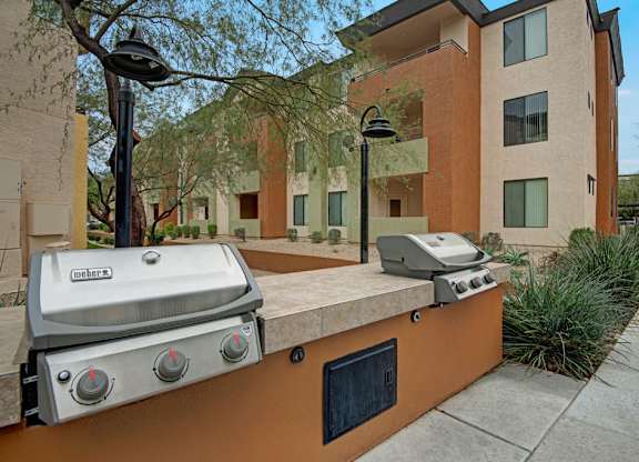 A Weber grill is on a concrete slab outside a building.