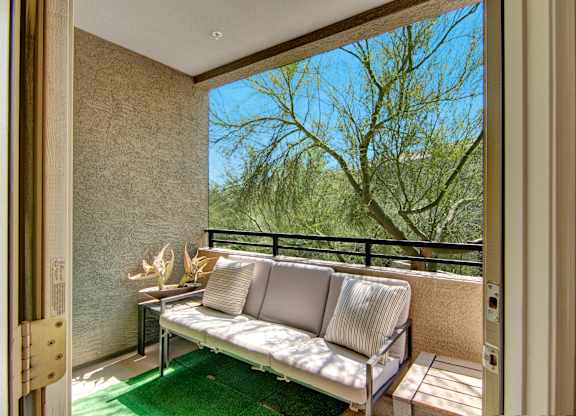 A white couch with pillows is on a balcony with a view of trees.