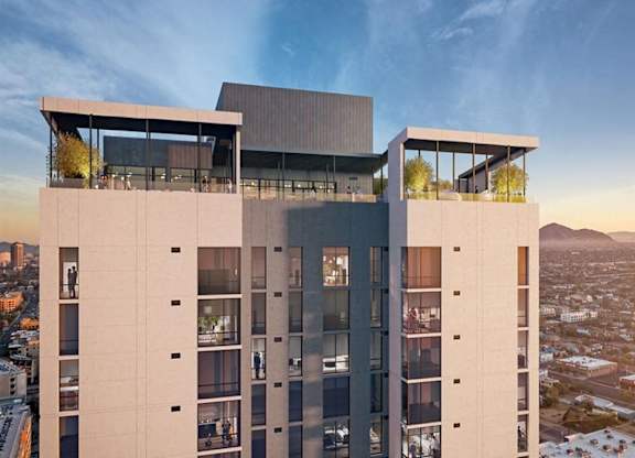 A striking high-rise exterior here at JOY on 4th showcasing modern architecture with clean lines, expansive glass balconies, and a rooftop amenity deck overlooking the city. Floor-to-ceiling windows reflect the sunset sky, while elevated lounge spaces crown the building with panoramic skyline and mountain views.
