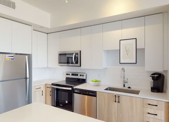 A modern and light-filled kitchen here at JOY on 4th showcasing sleek white upper cabinetry paired with warm wood lower cabinets and matte black hardware. Stainless steel appliances, smooth countertops, and a contemporary tile backsplash create a clean, streamlined look, while the deep undermount sink and generous prep space offer both style and everyday functionality.
