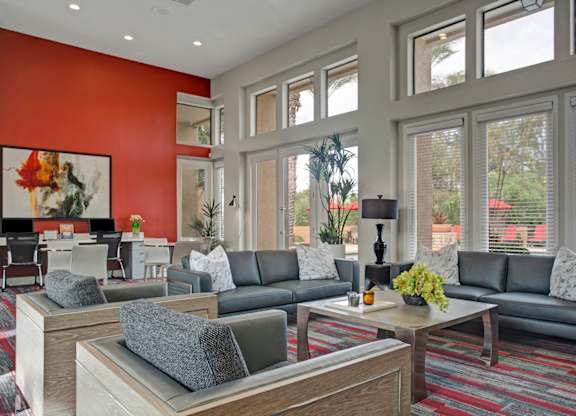 A bright clubhouse lounge here at Mirador featuring soaring ceilings and expansive windows that fill the space with natural light and views of the pool area. Contemporary leather sofas and armchairs surround a sleek coffee table, while a bold accent wall and nearby workspace create a stylish, inviting setting for relaxing or socializing.