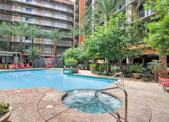 A small pool with a hot tub in the middle of a courtyard surrounded by trees and chairs.