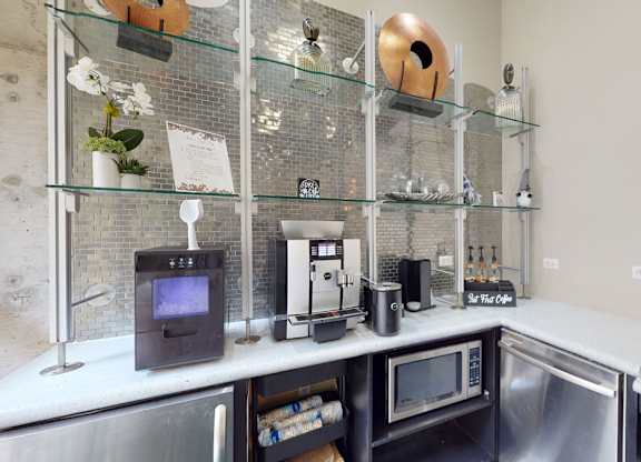 A modern kitchenette with stainless steel appliances and glass shelves.