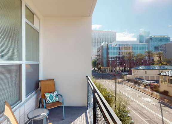 A balcony with a chair and a cushion overlooking a city street.