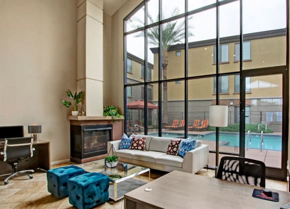 Spacious modern lobby here at Bolero Apartments with high glass windows overlooking a pool area. Features cozy seating, a fireplace, vibrant blue stools, and computer desks.