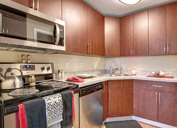 A stylish kitchen here at 3600 Brentwood with rich wood cabinets, speckled granite-style countertops, and stainless steel appliances including a microwave, dishwasher, and stove for a modern, functional space.