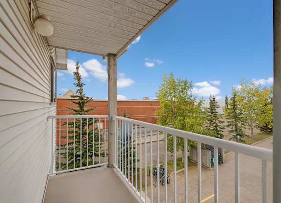 A private balcony here at Aspen Terrace with white railing and open views of trees and the surrounding community. A covered ceiling and outdoor light create a bright, breezy spot for fresh air.