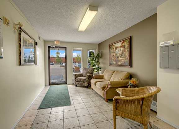 A welcoming lobby here at Aspen Terrace with tiled floors, a cozy seating area, and natural light from large front windows. A comfortable sofa, accent chairs, and warm wall art create an inviting first impression.