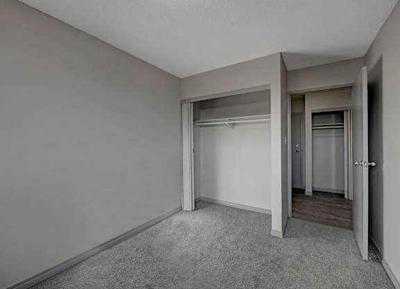 A bright bedroom here at Cedar Gardens with soft gray carpeting and clean, neutral walls, featuring a roomy open closet, a convenient hallway connection, and a simple layout that feels comfortable and easy to make your own.