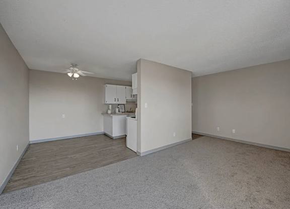 A spacious living area here at Cedar Gardens with an open layout and soft neutral tones, featuring plush carpeting, a separate dining nook with durable flooring, and a ceiling fan overhead for a comfortable, airy feel.
