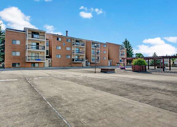 A well-maintained apartment building here at Gateway Square with private balconies, warm-toned exterior siding, open courtyard space, and landscaped planters under a bright blue sky.