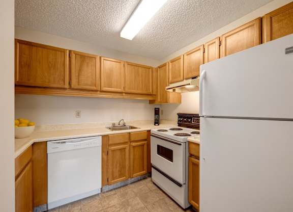 A bright kitchen here at Gateway Square featuring warm wood cabinetry, clean white appliances, and spacious counters with a stainless sink, creating a simple and functional space for everyday cooking.
