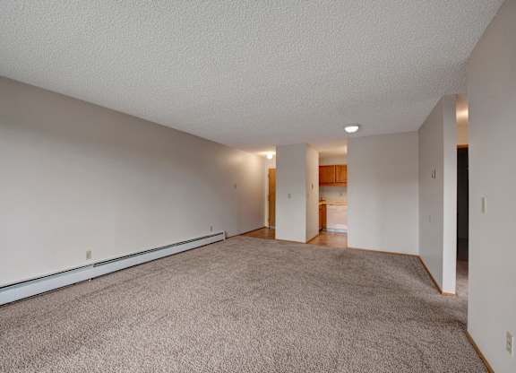 A bright open living space here at Gateway Square featuring soft neutral walls, plush carpet flooring, and a long layout that offers plenty of room to relax, with a cozy flow leading into the kitchen area for easy everyday living.