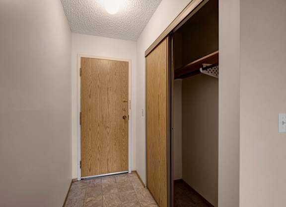 A bright entryway here at Gateway Square featuring a clean tiled floor, warm wood-toned front door, and a spacious closet for easy storage, creating a simple and welcoming first impression.