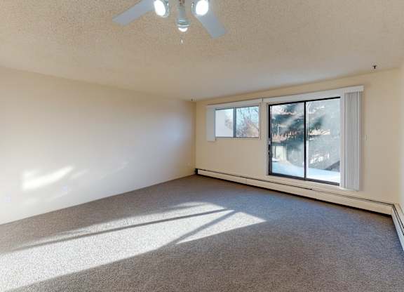 A bright living area at Lakewood Heights with plush carpet, neutral walls, ceiling fan lighting, and a large sliding window that brings in natural light and creates a comfortable, open feel.