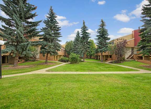 A peaceful courtyard at Lakewood Heights featuring manicured green lawns, mature trees, walking paths, and a quiet community setting that offers a relaxed, park-like vibe right outside your door.