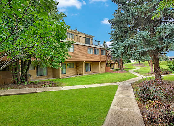 A tree-lined walkway at Lakewood Heights featuring lush green lawns, mature landscaping, and convenient ground-level access that creates a calm, neighborhood-style outdoor setting.
