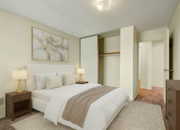 A calm, inviting bedroom here at Lakewood Heights with soft neutral walls, plush carpet, a comfortable bed with layered bedding, warm bedside lighting, and a sliding-door closet that adds convenient storage.