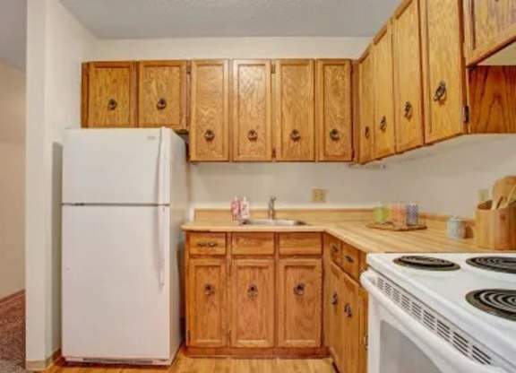 Small kitchen here at Madison Park Apartment Homes with a white fridge, wooden cabinets, and a beige countertop. Includes a sink, stove, and neatly arranged kitchen items, conveying a cozy feel.