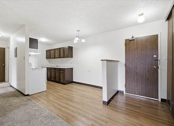 A kitchen area with a white fridge, wooden cabinets, and a brown door.