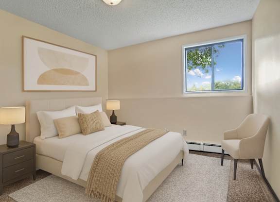 A serene bedroom here at Ventana featuring a queen-sized bed with crisp white bedding, layered neutral pillows, and a soft beige throw, complemented by matching bedside tables with lamps, abstract wall art above the headboard, plush carpeting, a cozy accent chair, and a bright window bringing in natural light.