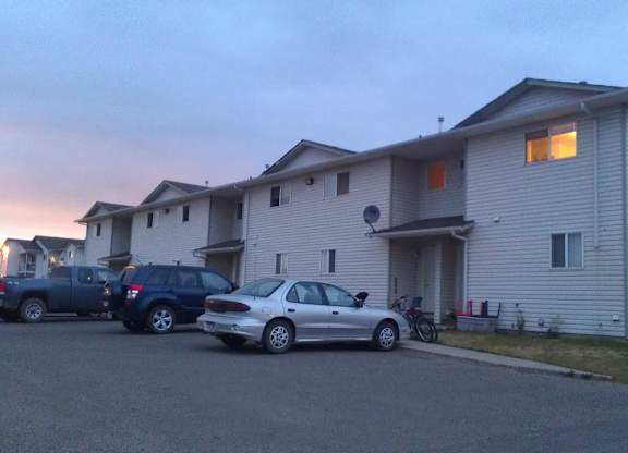 A peaceful exterior view here at Willowview Terrace showing a row of townhome-style buildings with light siding and convenient parking right out front. A soft evening sky and warm window lighting add a calm, welcoming feel to the community.