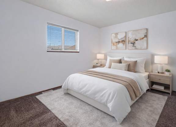 A bright and simple bedroom here at Willowview Terrace featuring a neatly made bed with crisp white bedding, neutral accent pillows, and a soft throw blanket. Matching nightstands with modern lamps sit on each side, with minimal decor and two framed abstract art pieces above the headboard. A large window and plush carpet help create a cozy, inviting space.