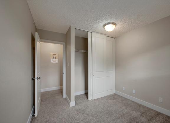 A simple bedroom here at Wyndham Crossing with soft neutral walls, plush carpet flooring, and a warm ceiling light for a comfortable layout. A sliding-door closet with hanging storage sits beside the open doorway leading into the hallway.
