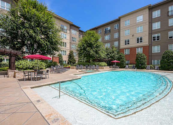 A large swimming pool surrounded by a patio with chairs and umbrellas.