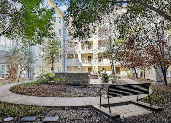 A bench sits in front of a building with a circular garden in the foreground.