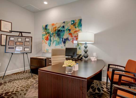 A room with a desk, chair, and painting on the wall.