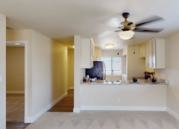 Modern kitchen and dining area here at Vista View Apartment Homes with open layout. White cabinets, granite countertops, black appliances, ceiling fan, and window with blinds create a cozy atmosphere.