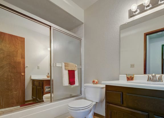 Modern bathroom here at The Continental Apartments with a tiled shower, glass door, and white sink. A towel hangs over the shower door, and the vanity features a large mirror and lights.