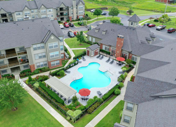 an aerial view of a large swimming pool with umbrellas in front of an apartment complex
