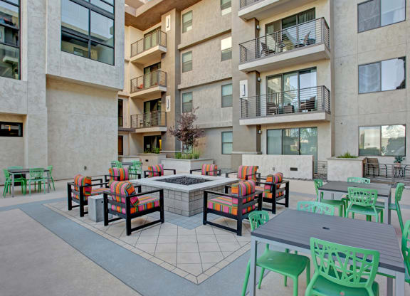 Modern apartment courtyard here at Escape Apartments with colorful striped chairs around a central fire pit, surrounded by green chairs and tables. Building backdrop with balconies.