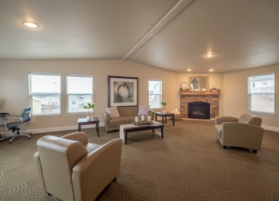 Spacious resident lounge here at Four Seasons Apartments with beige armchairs, a stone fireplace, large windows, abstract art, and patterned carpet, conveying a cozy and elegant ambiance.