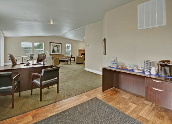 Office reception area here at Four Seasons Apartments with modern decor. Dark wood desks and chairs on green carpet. Refreshment station on the right. Bright, welcoming atmosphere.
