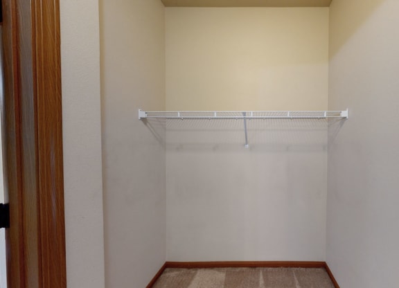 Empty beige closet here at Grand River Estates Apartment Homes with a wire shelf mounted on the back wall. The doorframe is wooden, and the floor is carpeted. Simple, tidy space.