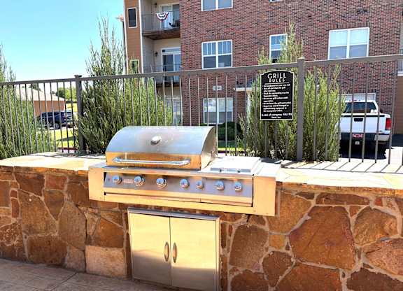 A grill is on a stone wall with a sign behind it.
