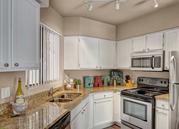 Modern kitchen here at The Hawthorne Apartments with stainless steel appliances and white cabinets. Stone countertops, decorative "EAT" letters, and a wine bottle create a cozy, inviting atmosphere.