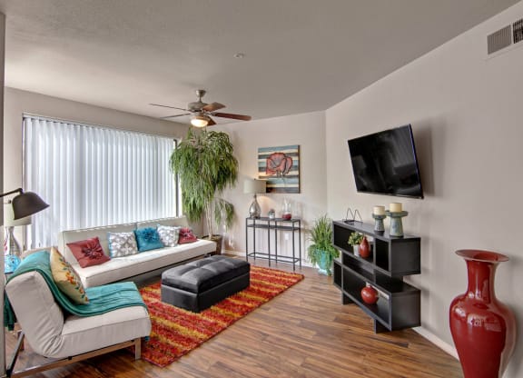 Modern living room here at The Hawthorne Apartments with a white sofa, colorful pillows, and a striped rug. A large plant, wall painting, and wall-mounted TV add a cozy feel.