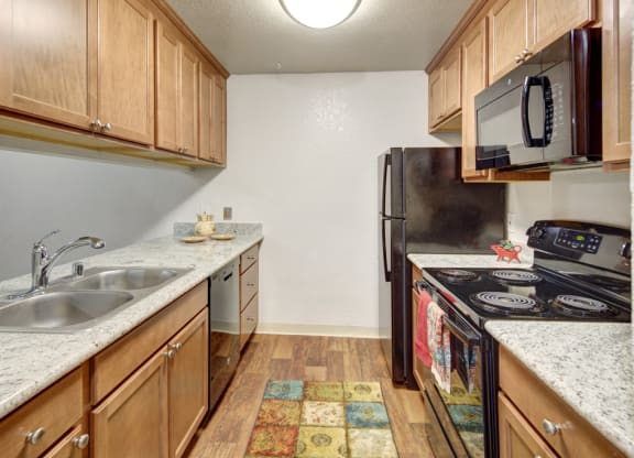 Modern kitchen here at Hillside Chalet Apartments with light wood cabinets, granite countertops, and stainless steel appliances. A colorful rug adds warmth, with an inviting, tidy feel.