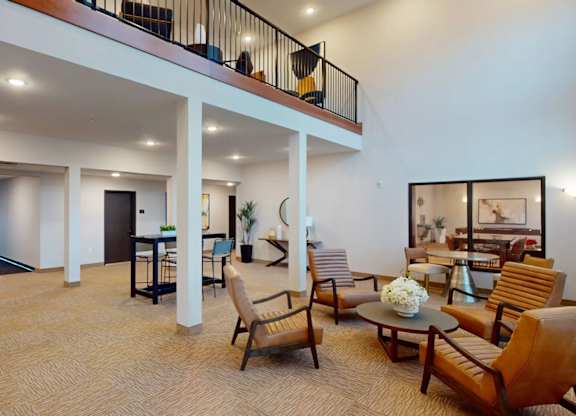 A modern clubhouse lobby here at Club at Heritage with high ceilings, cozy seating areas, and warm lighting. A lofted second level and open layout create a spacious, inviting environment for relaxing or socializing.