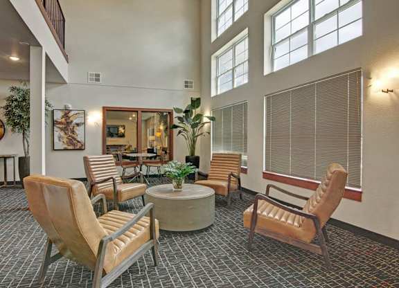 A stylish clubhouse lounge here at Club at Heritage with high ceilings, large windows, and comfortable seating. A central table and modern décor create a warm, inviting space ideal for relaxing or gathering.