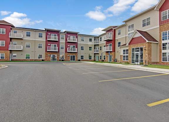 A community exterior here at Club at Heritage with multi-story buildings, private balconies, and a clean, spacious parking area. A welcoming entrance and modern design create a well-maintained and inviting atmosphere.